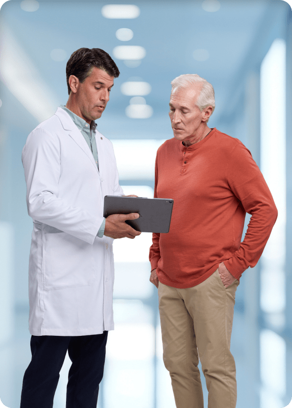 Doctor in white coat and patient in red shirt reviewing medical information on a tablet together.
